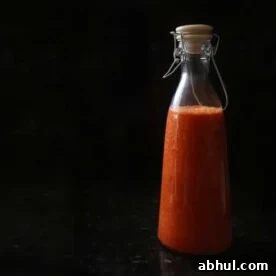 A tall jar of red hot sauce, against a stark black background.