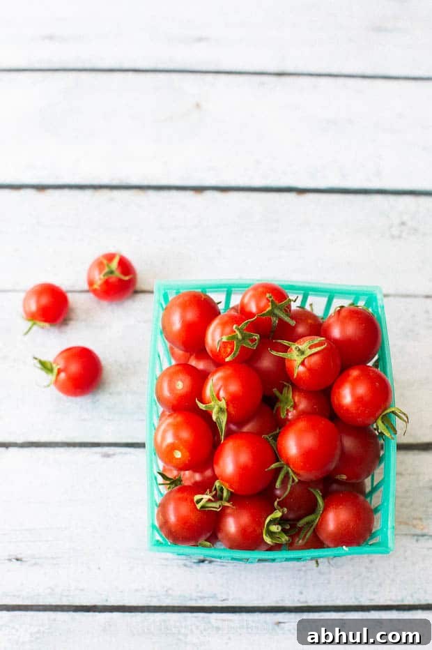 A green plastic tub of fresh red cherry tomatoes sits on a table. A few tomatoes have fallen out.
