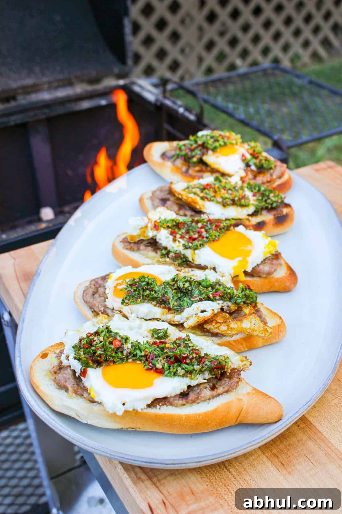 side view of buns layered with ground sausage, egg, and chimichurri on a plate