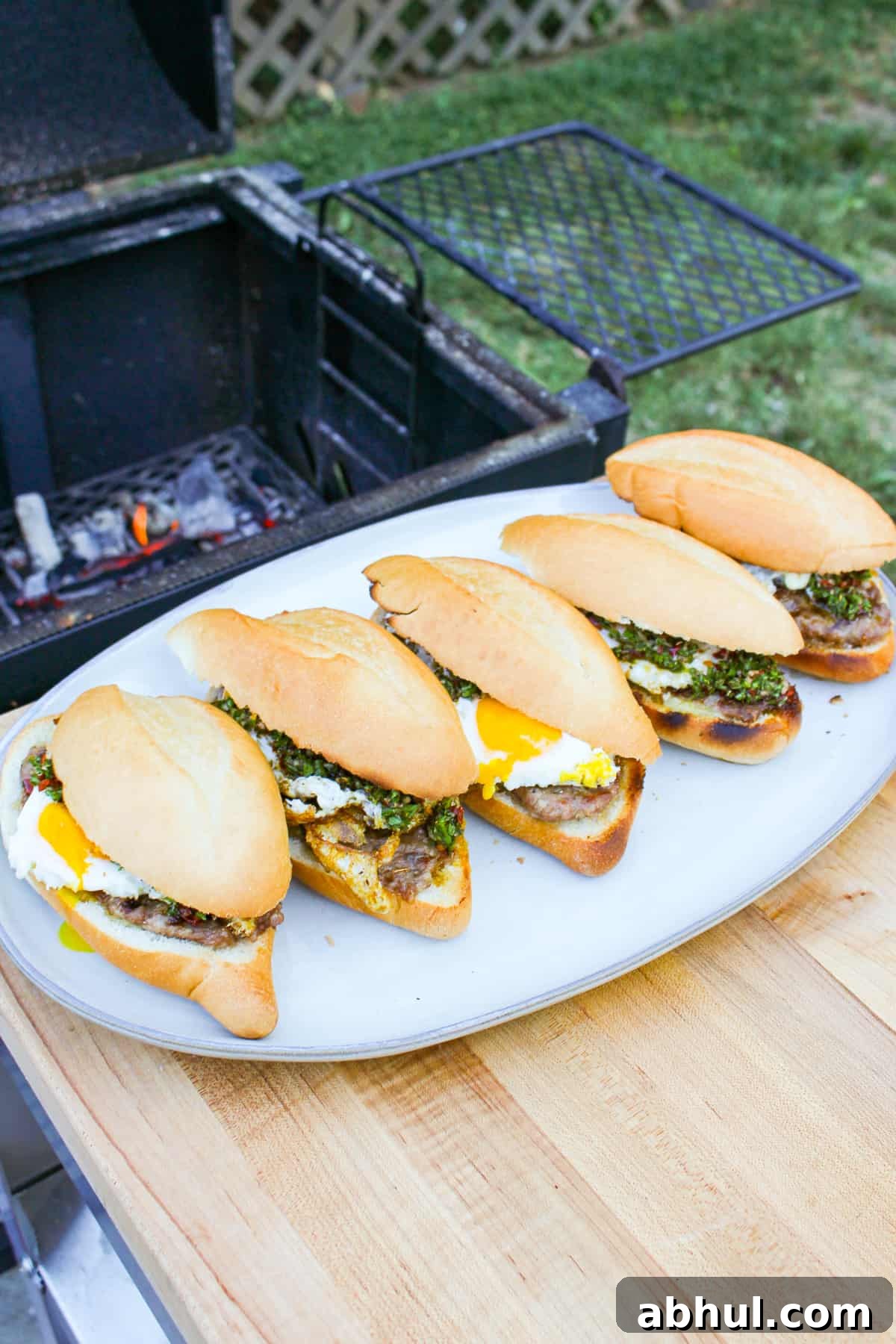 finished cheese stuffed sausage sandwiches on a white platter next to a grill