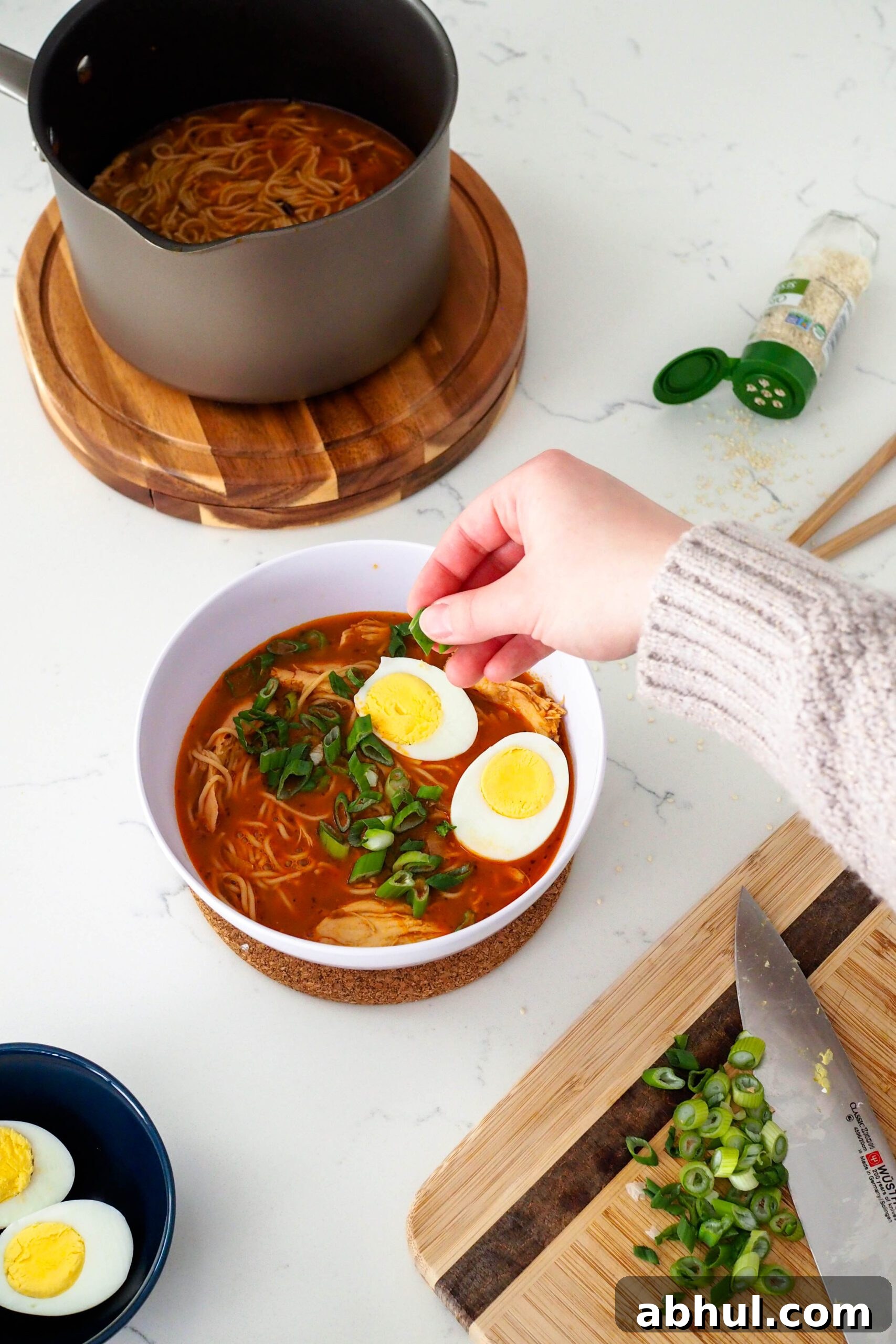 Spicy Gochujang Chicken Ramen Recipe for Quick Weeknights 2 A hand adds sliced green onions on top of gochujang ramen.
