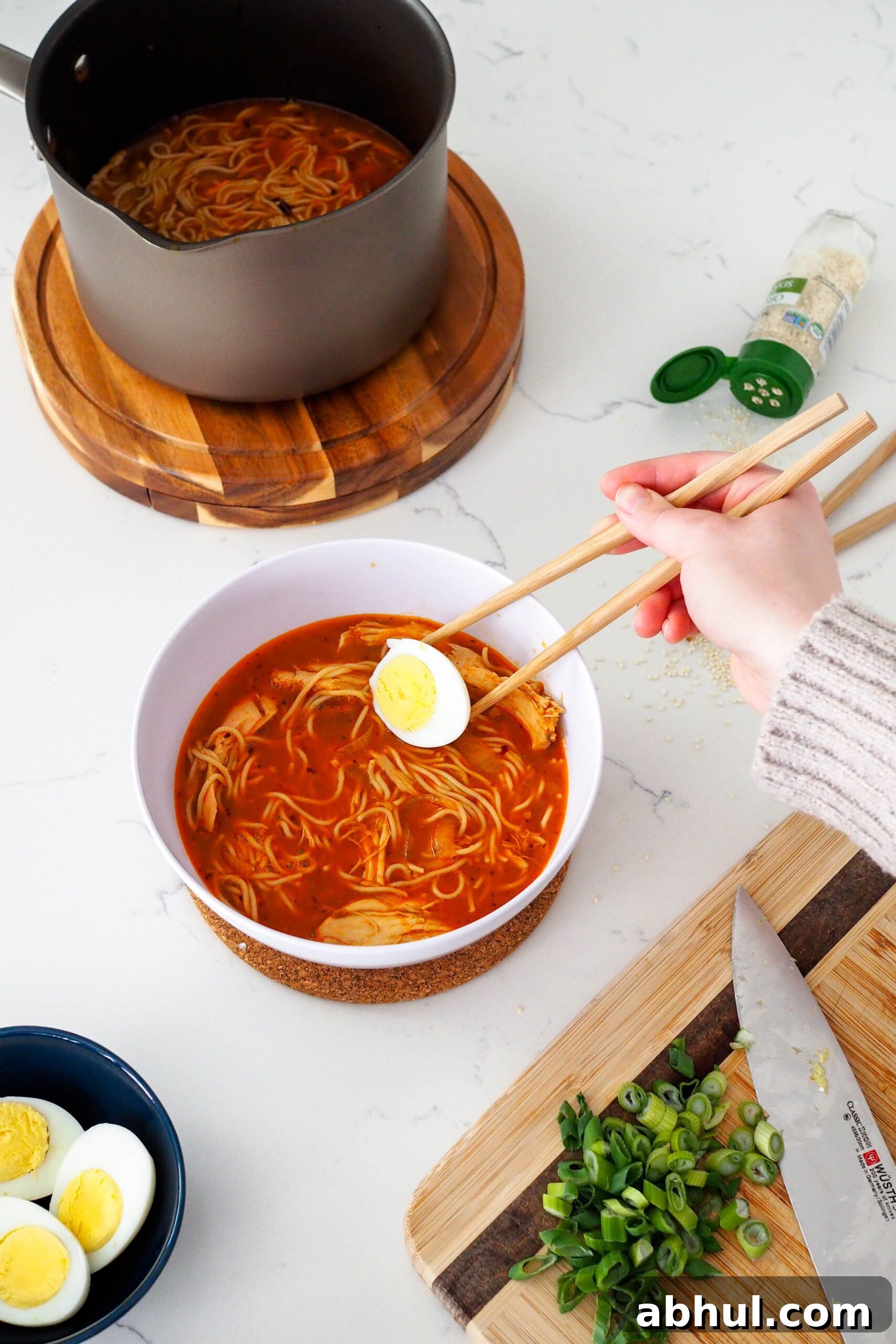 Spicy Gochujang Chicken Ramen Recipe for Quick Weeknights 11 A hand places half of a boiled egg into a bowl of ramen with chopsticks.