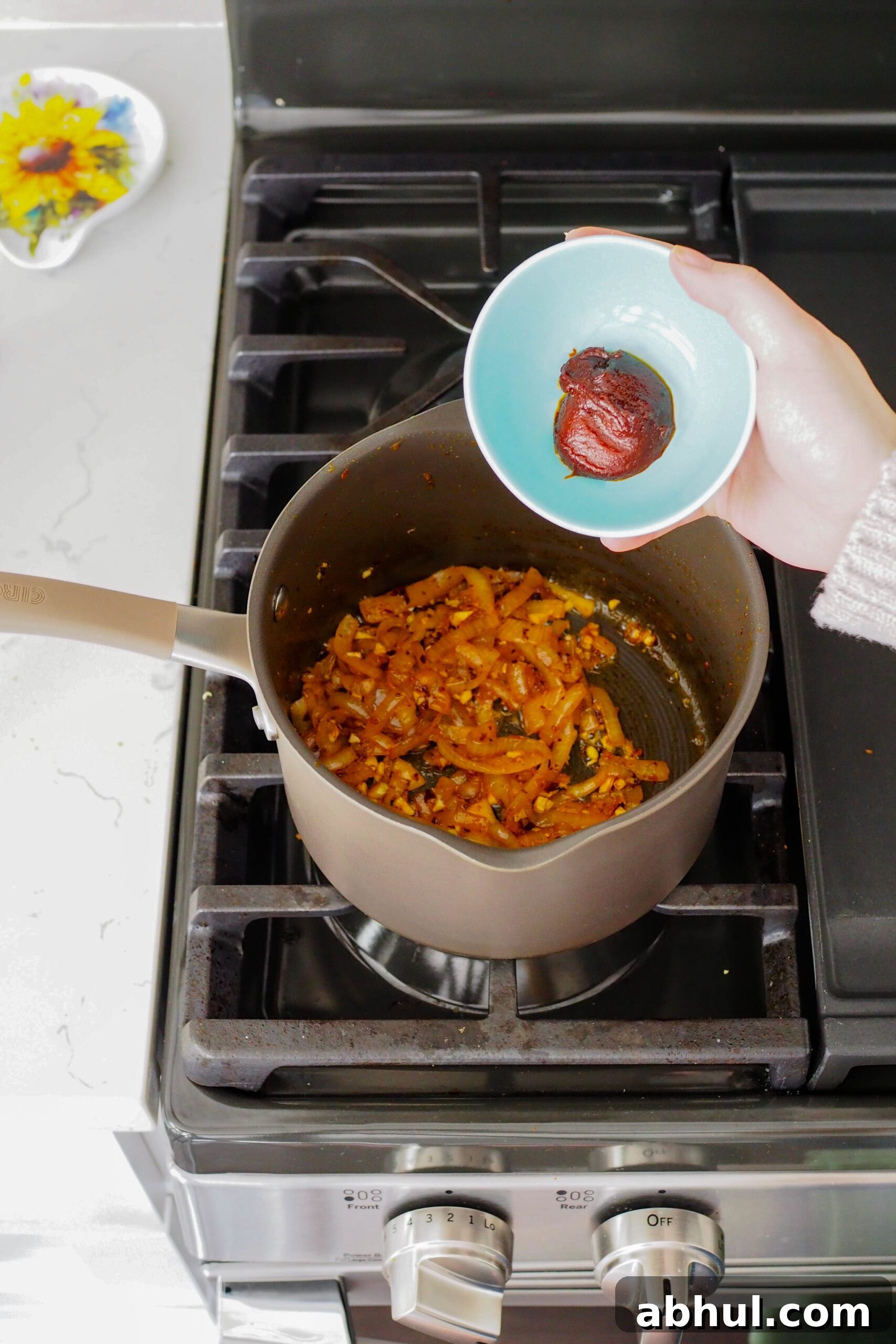 Spicy Gochujang Chicken Ramen Recipe for Quick Weeknights 8 A hand pours gochujang into a pot of caramelized onions.