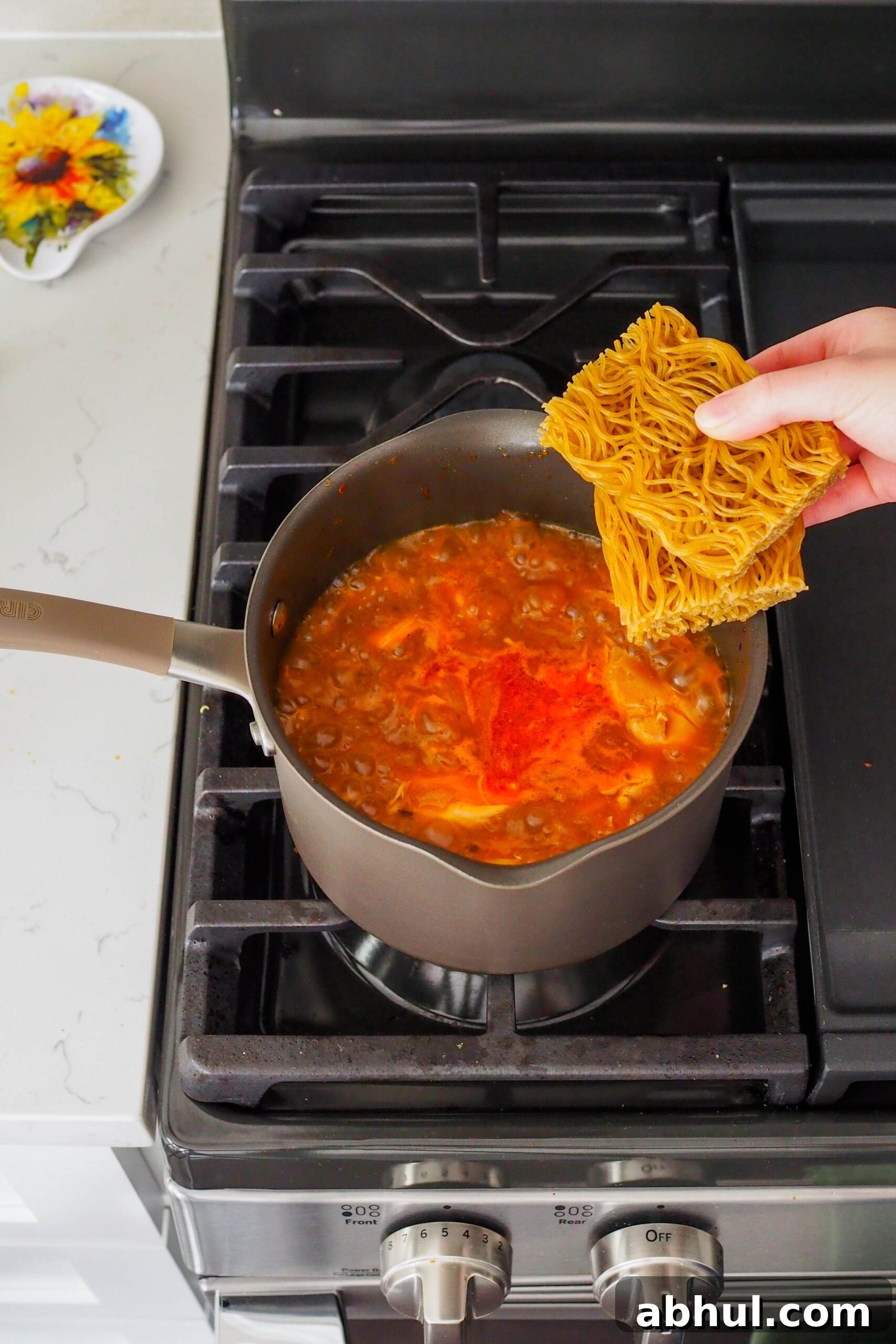 Spicy Gochujang Chicken Ramen Recipe for Quick Weeknights 10 A hand places two cakes of dried ramen noodles into ramen broth.