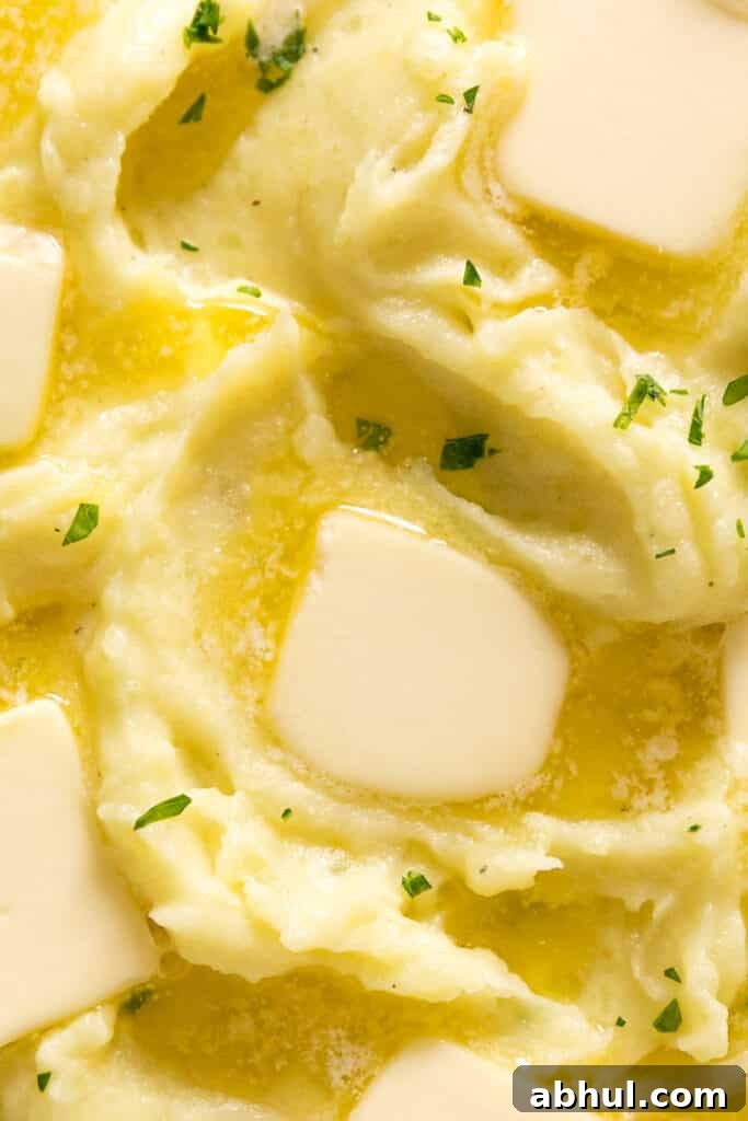 An overhead close up of the top of a bowl of this garlic mashed potatoes recipe with chopped parsley and melting butter pats on top of it.