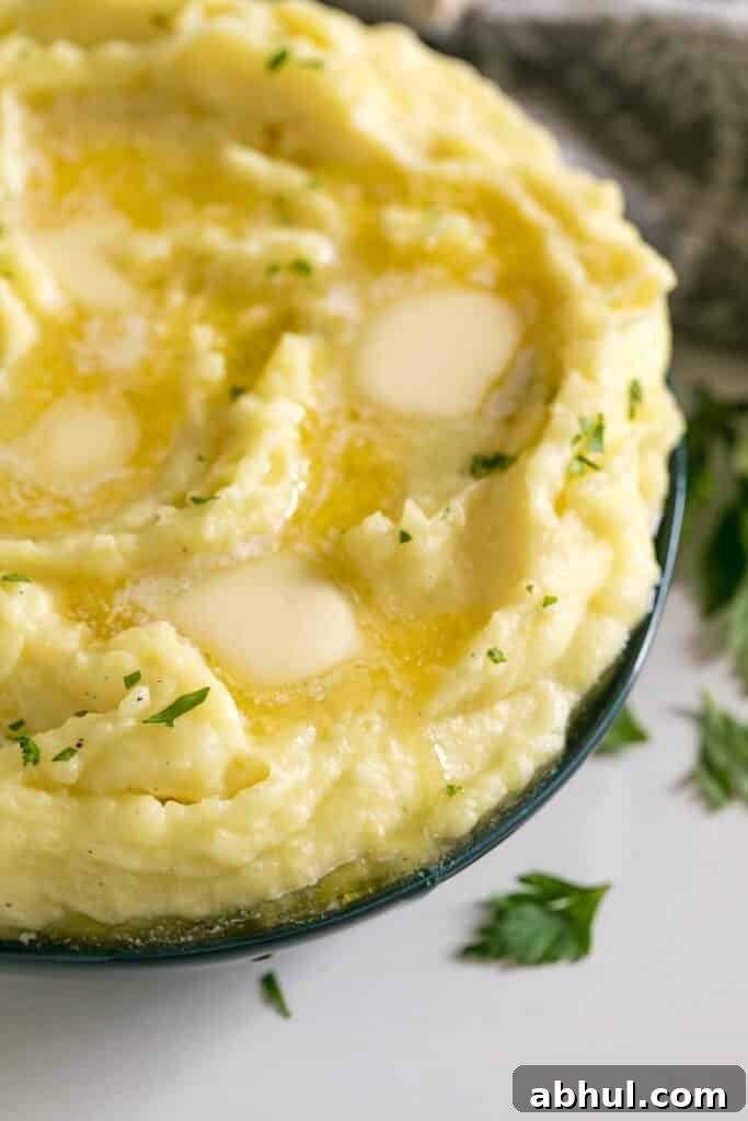 The side of a bowl of mashed potatoes with melting butter pats on top of it in a blue bowl.