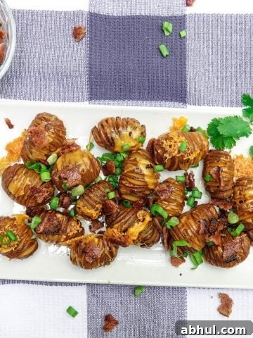 Smoked hasselback potatoes topped with cheese, bacon, and green onions on white dish