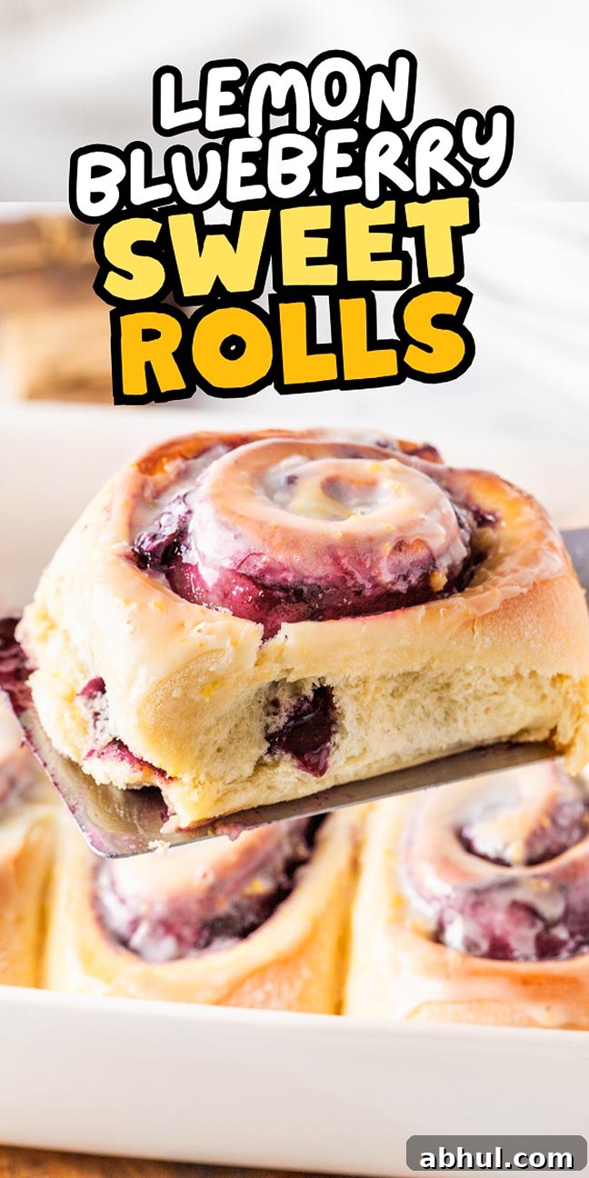A lemon blueberry sweet roll teeters delicately on a spatula, hovering above a baking dish filled with more mouthwatering lemon blueberry sweet rolls.