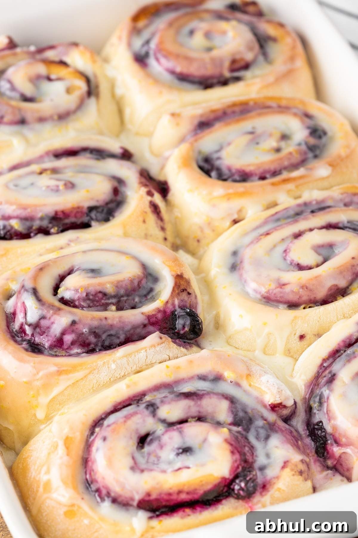 A close-up of a tray with freshly baked lemon blueberry sweet rolls, topped with a luscious glaze.
