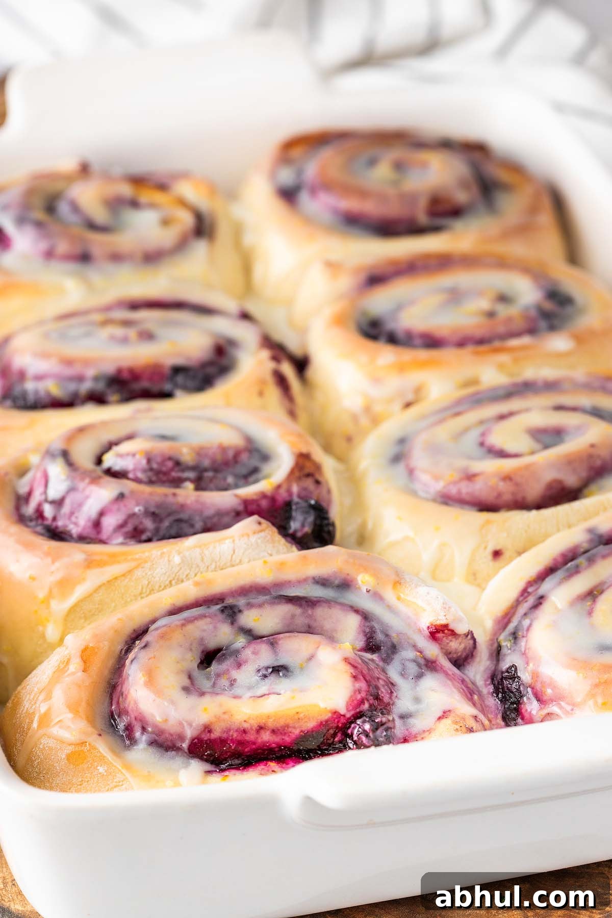 A close-up of freshly baked lemon blueberry sweet rolls with a cinnamon glaze in a white baking dish.