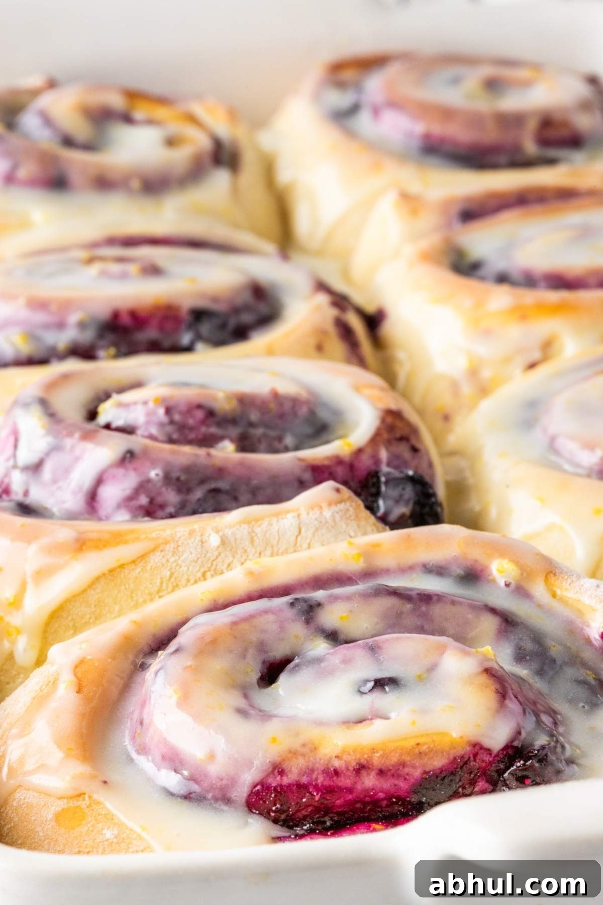 Close-up of freshly baked lemon blueberry sweet rolls topped with a light glaze in a baking dish.