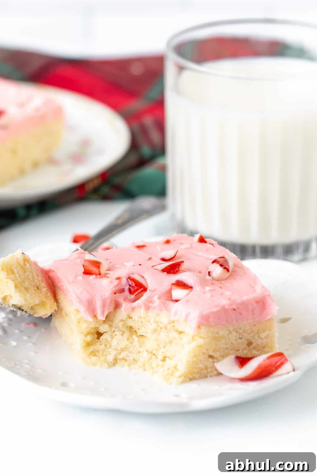 Candy cane sugar cookie bar with bite taken out, with glass of milk