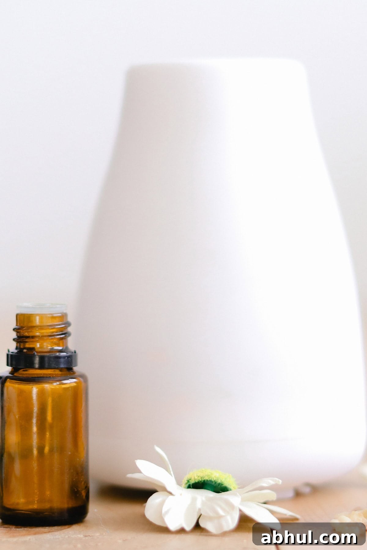 A minimalist essential oil diffuser with a delicate white flower, and an amber-colored essential oil bottle on a wooden surface.