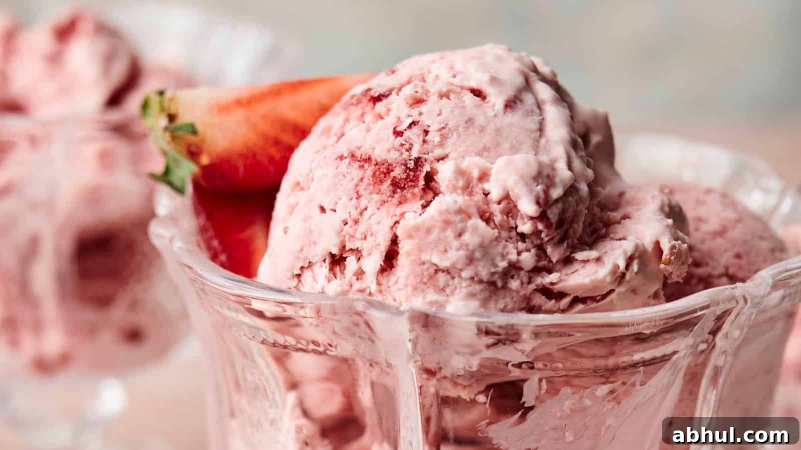 Close-up of scoops of strawberry ice cream in a glass dish, garnished with a fresh strawberry.