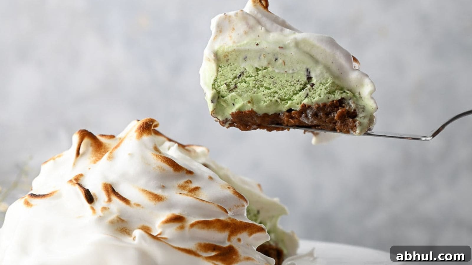 A slice of baked Alaska with a toasted meringue exterior and green ice cream center being lifted from the dessert.