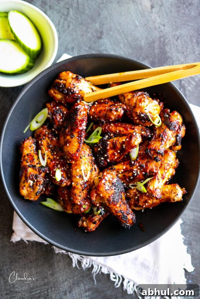 spicy grilled Asian style chicken wings in black bowl with bamboo tongs