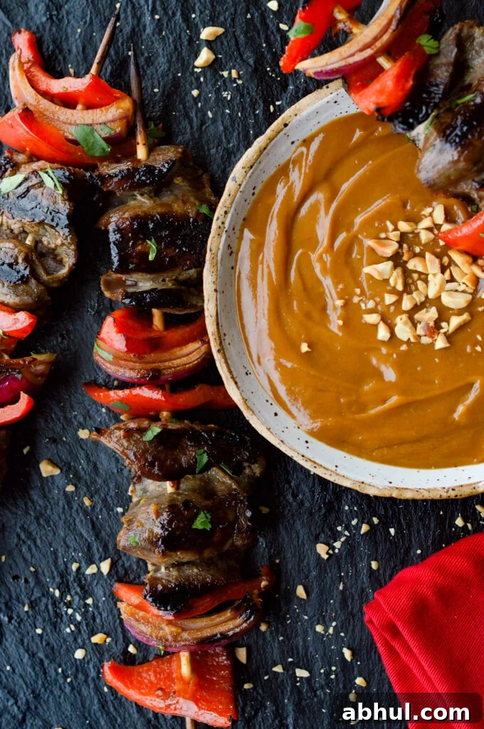 Beef Satay -Flank steak, red onions and red bell peppers on wooden skewers with a bowl of peanut sauce next to them.