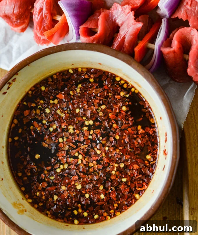 A closeup photo of marinade for beef satay. Flank steak, red onion and red bell pepper skewer sits next to it.