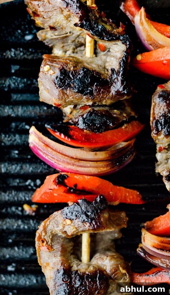 Beef Satay - A closeup view of flank steak, red onions, red bell peppers on wooden skewers are on an Electric Grill.