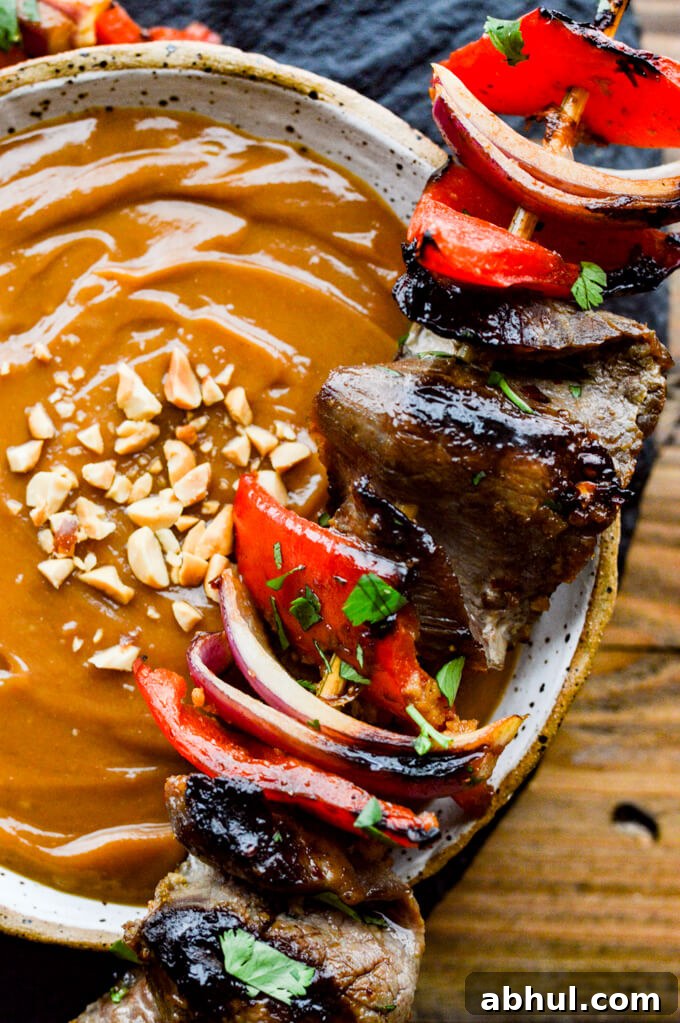 Beef Satay - A closeup photo of a bowl of peanut sauce with a flank steak skewer sitting on the bowl.