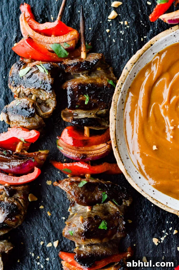 Beef Satay - Flank steak, red onions and red bell peppers on wooden skewers with a bowl of peanut sauce next to them.