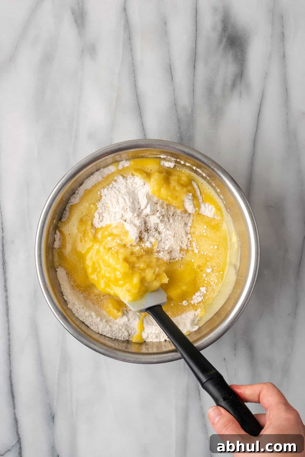 Mashed banana and egg mixture being folded into the dry ingredients with a spatula.