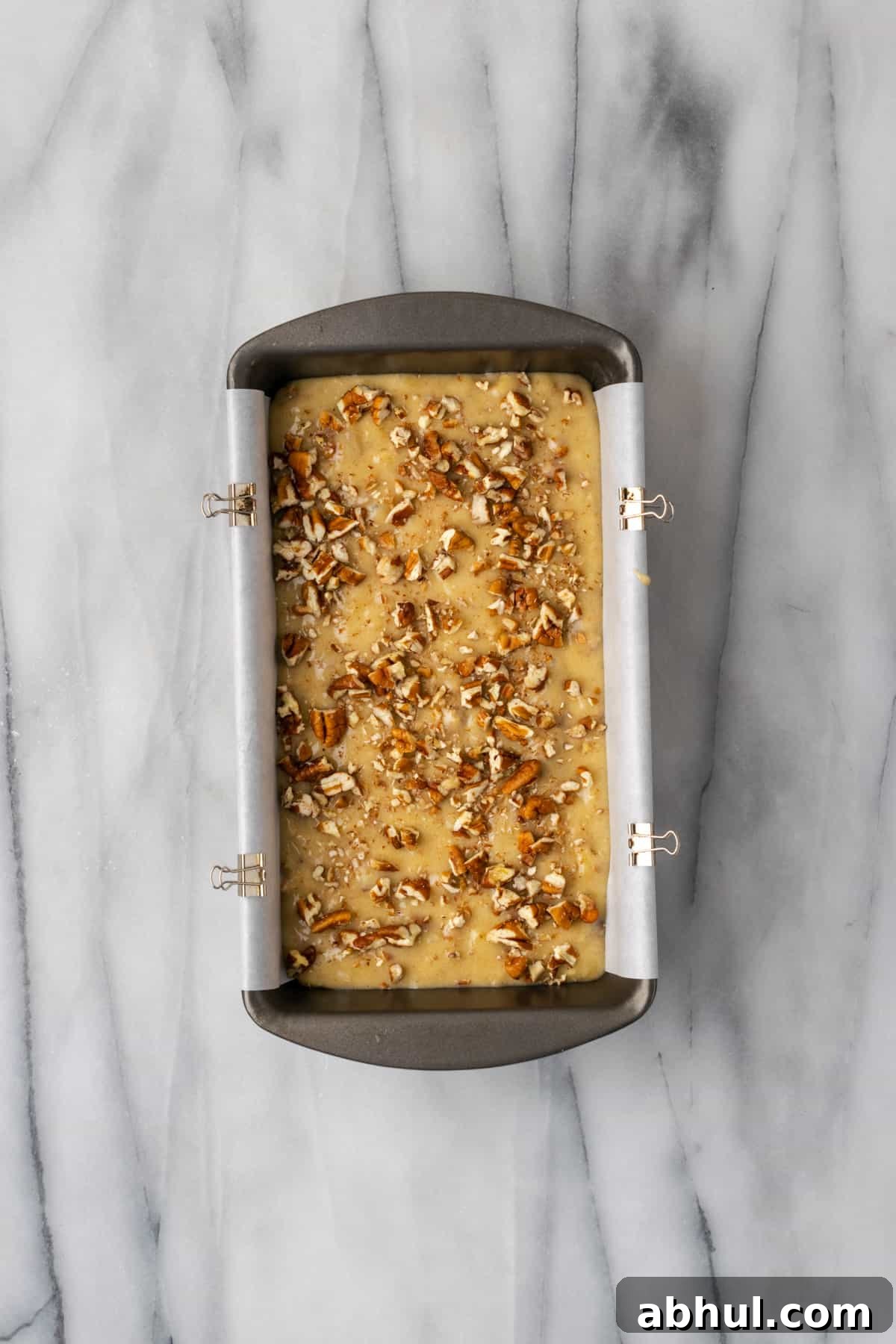 Unbaked banana bread topped with chopped pecans in a parchment lined baking tin.