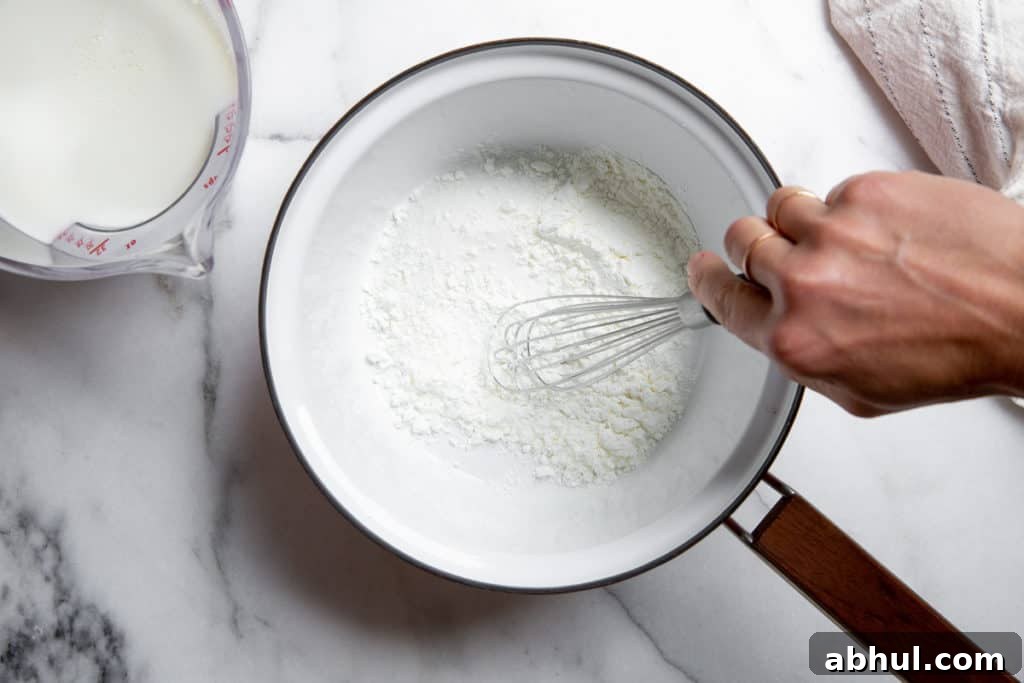 Homemade Gluten-Free Vanilla Pudding Recipe from Scratch 5 Hand whisking sugar, cornstarch and salt in a saucepan, with milk alongside.