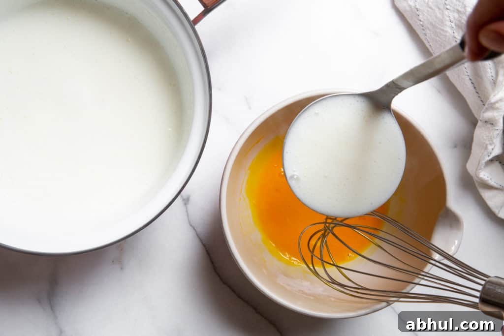 Homemade Gluten-Free Vanilla Pudding Recipe from Scratch 6 Process shot showing a ladle pouring hot milk into a bowl of egg yolks.