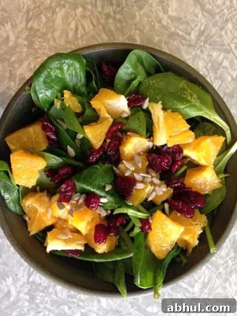 Bowl of spinach salad topped with peaches, cranberries, and sunflower seeds.