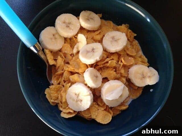 A blue bowl of cornflake cereal topped with sliced bananas.