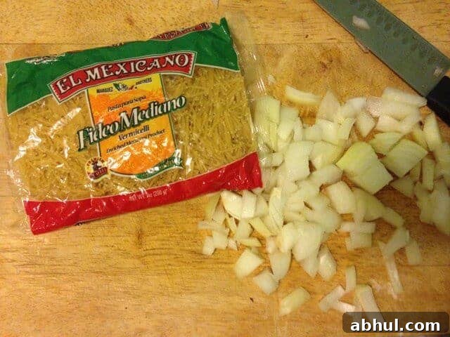 A bag of spaghetti pieces on a wood cutting board next to diced onion.