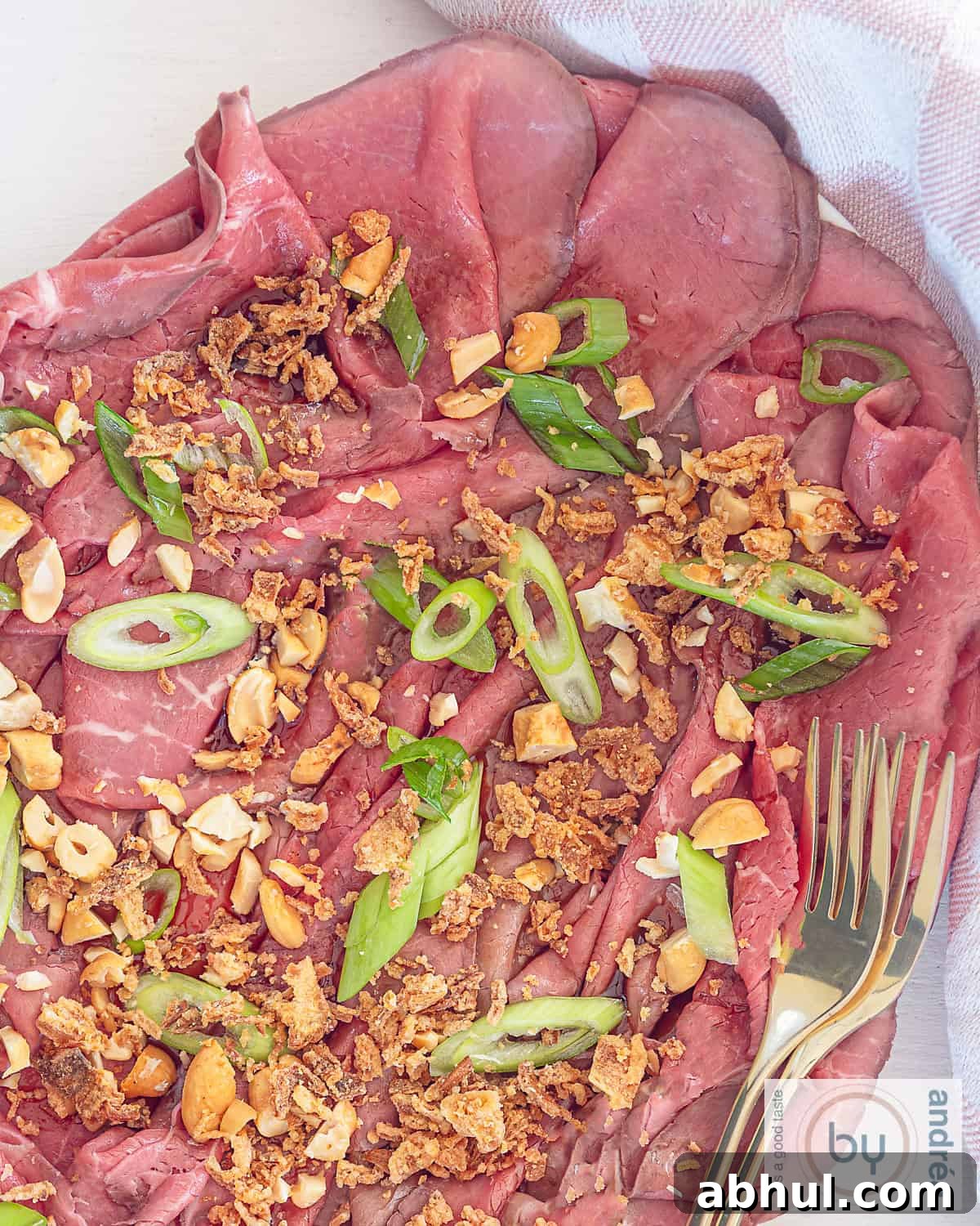 A top-down photo of a platter of roast beef with Asian-style garnish and dressing in the form of a carpaccio appetizer