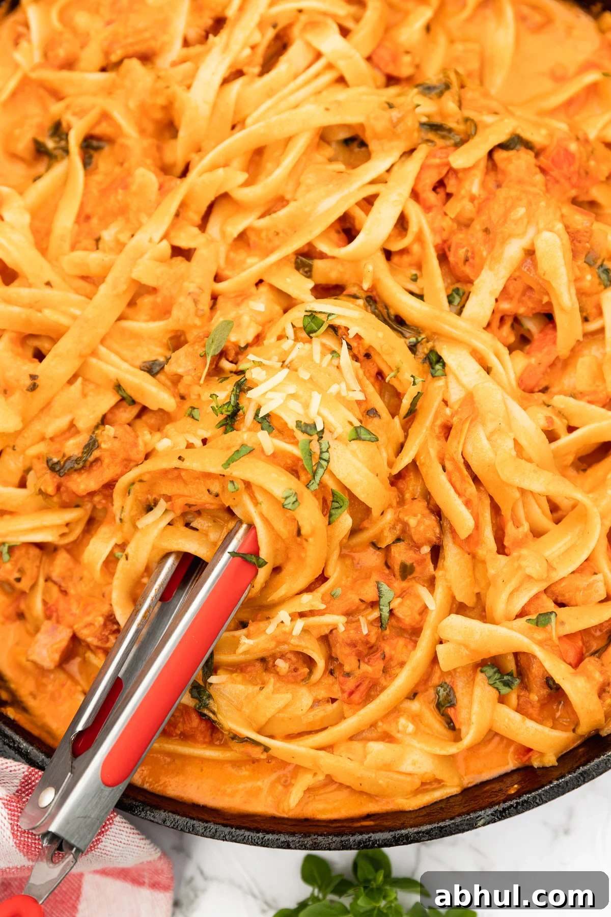A closeup of the pan of pasta with tongs in it and finely chopped basil and parmesan on top.