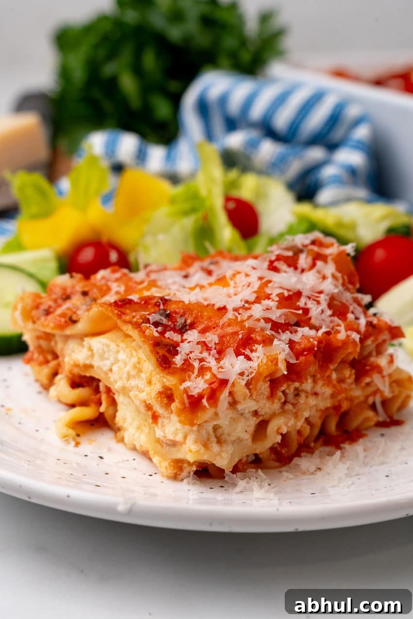A slice of lasagna rosa on a white plate with a simple salad on the side