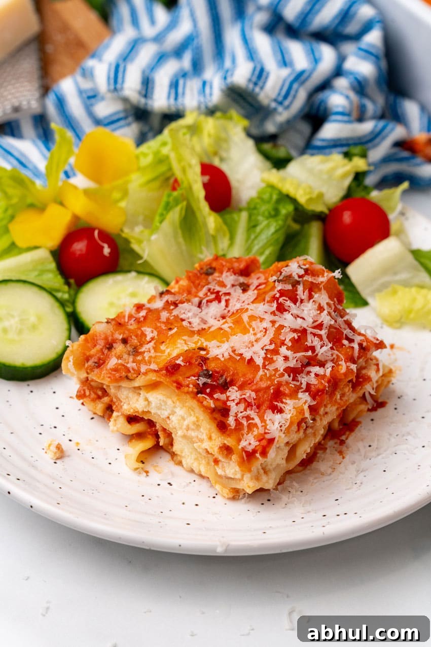 A slice of lasagna rosa on a white plate with a simple salad on the side