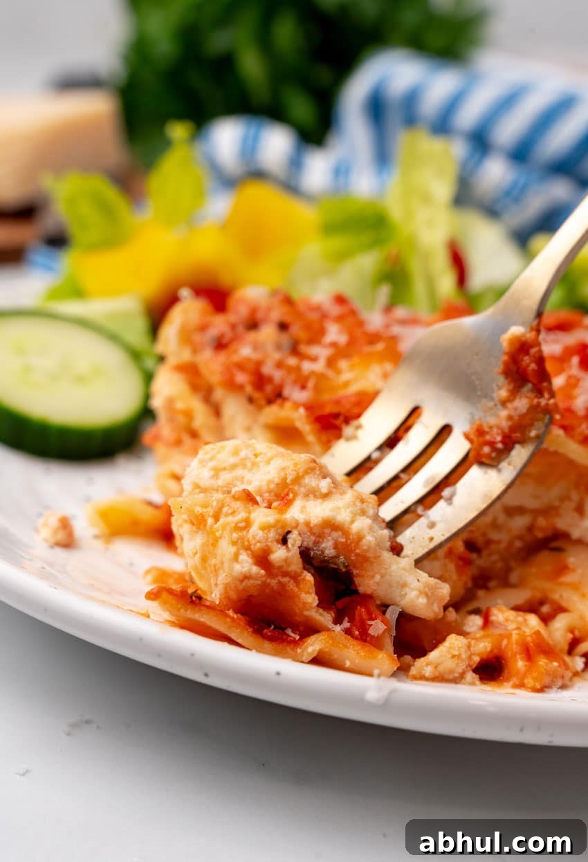 a silver fork scooping a piece of a slice of lasagna rosa off a white plater