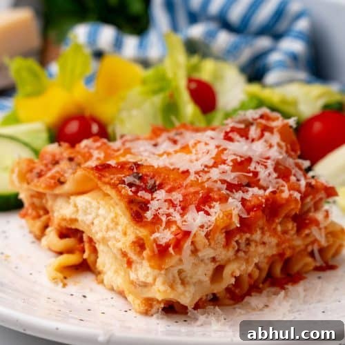 A slice of lasagna rosa on a white plate with a simple salad on the side