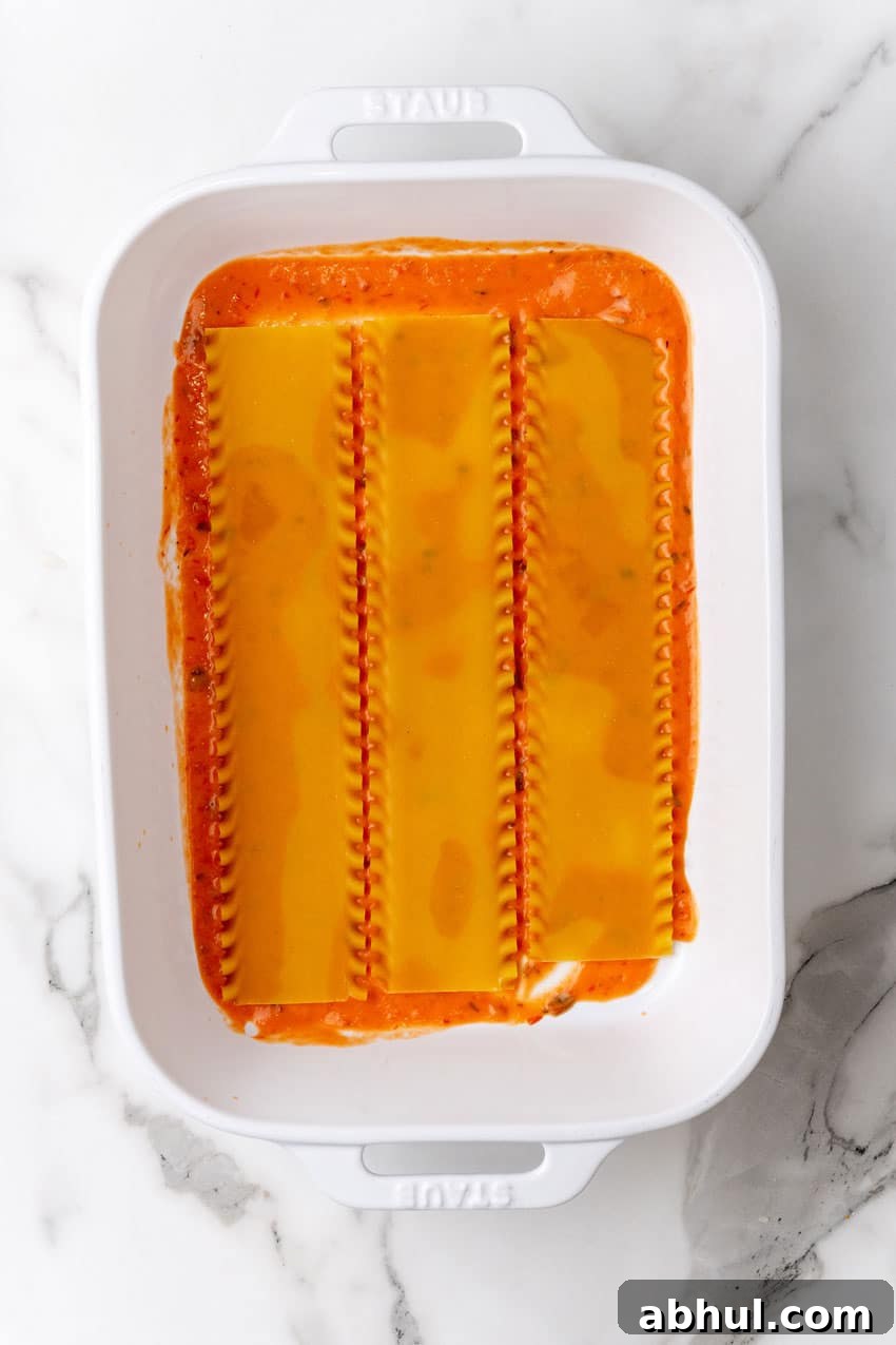 uncooked lasagna noodles arranged in a row over a blush sauce in a white baking dish