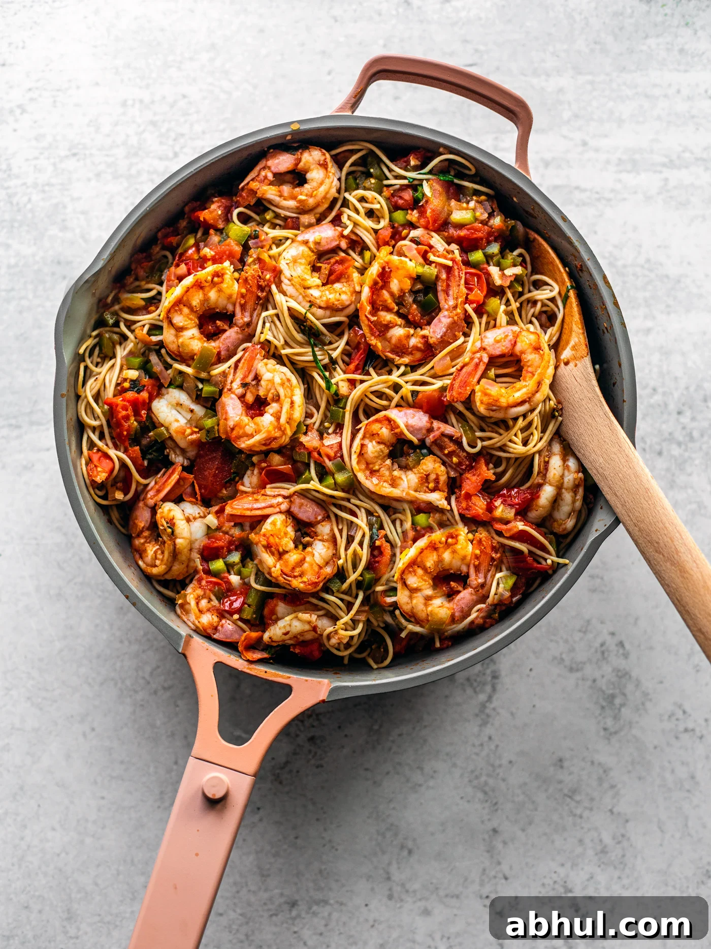 Pan brimming with pasta and Cajun shrimp with a wooden serving spoon.
