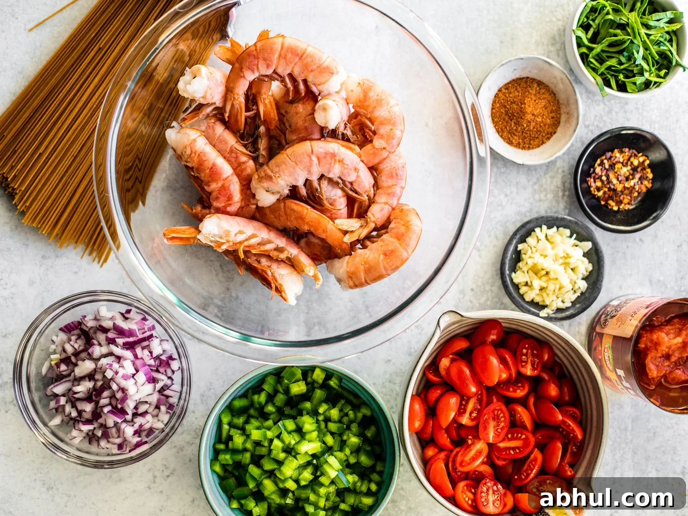 Bowl of shell-on shrimp surrounded by bowls of chopped and prepared ingredients.