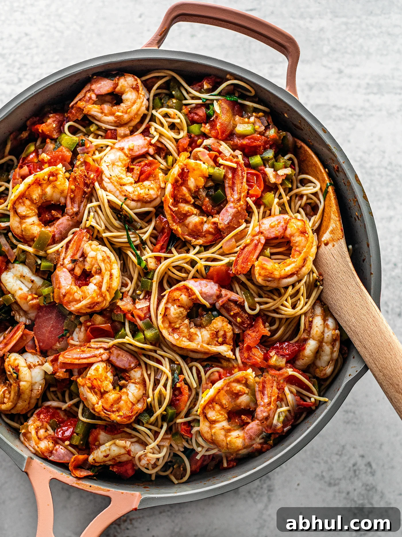 Close up of pan brimming with pasta and Cajun shrimp with a wooden serving spoon.