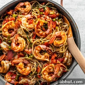 Close up of pan brimming with pasta and Cajun shrimp with a wooden serving spoon.