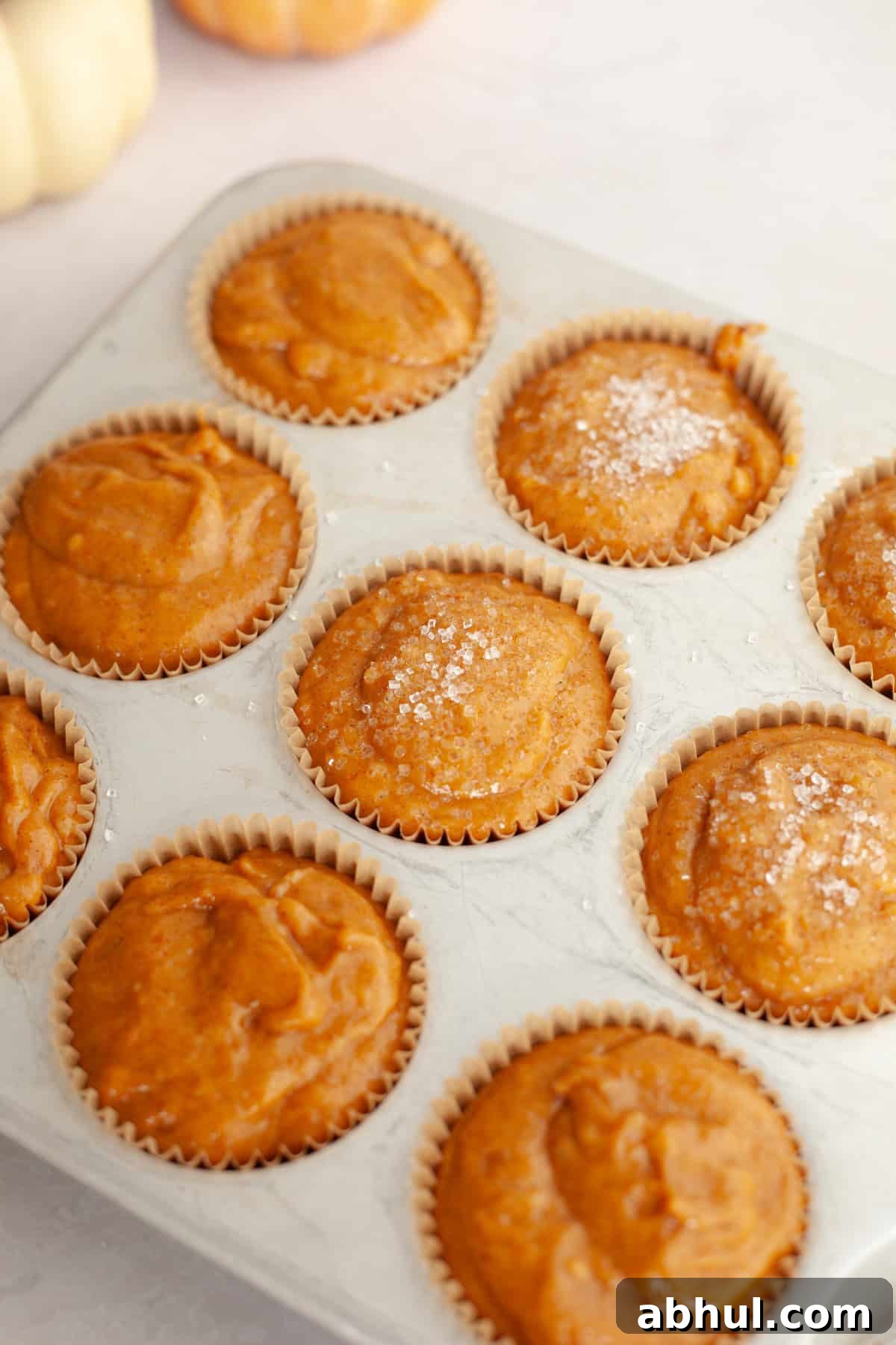 One-Bowl Pumpkin Sour Cream Muffins: Moist Fall Recipe 6 Unbaked pumpkin muffins in a muffin pan, some are topped with sparkling sugar.