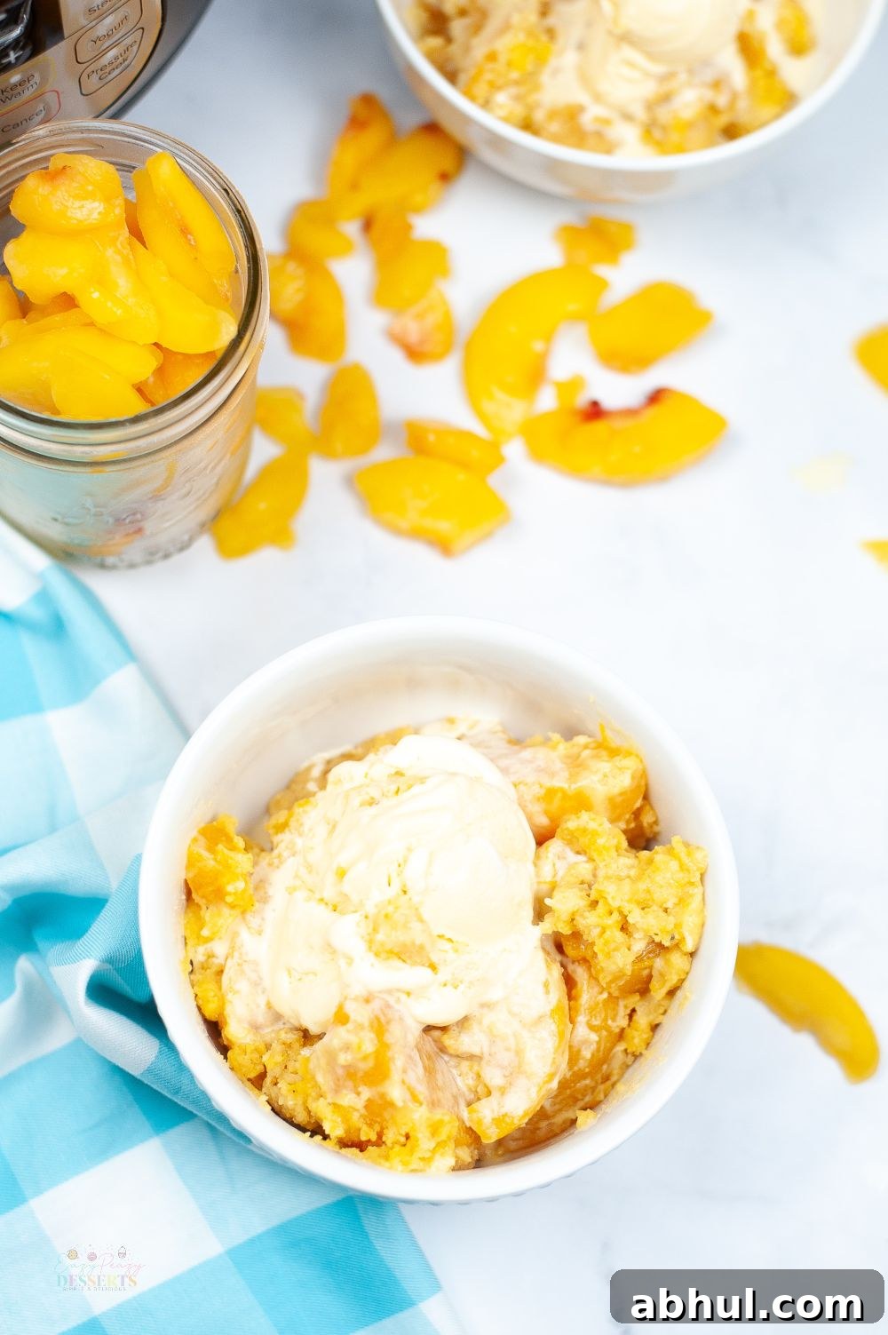 Image of instant pot peach cobbler in a white bowl, topped with vanilla ice cream