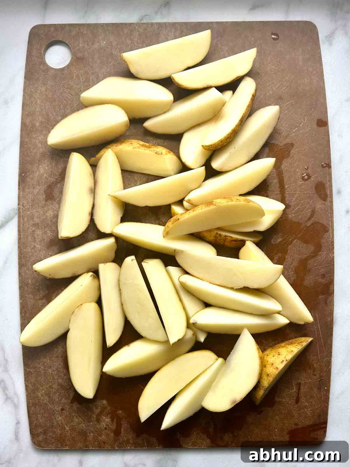 potatoes cut into wedges on cutting board.