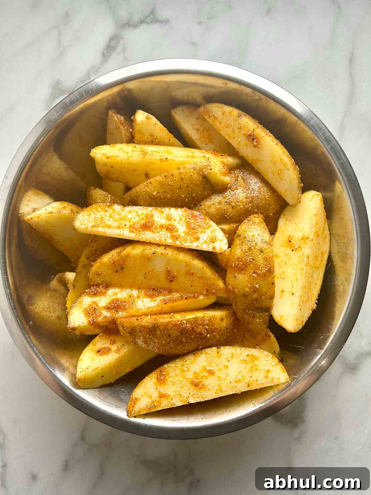 potato wedges tossed with oil and spices in bowl.