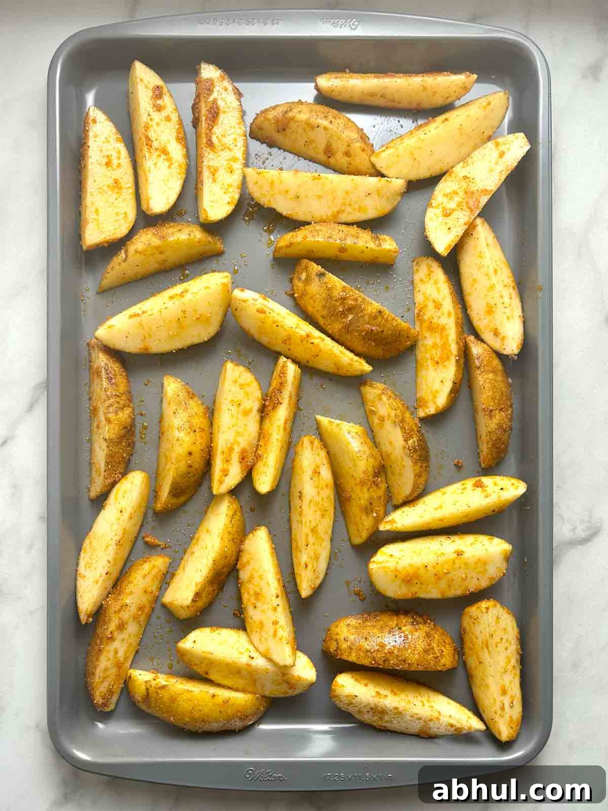 potato wedges spread on baking sheet before baking.