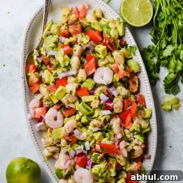 avocado shrimp ceviche salad on white serving dish beside a bunch of fresh cilantro and lime halves on gray background.