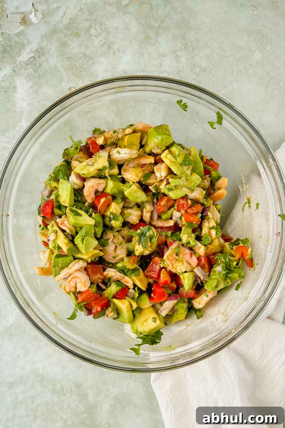tossed avocado shrimp ceviche in a glass mixing bowl on green background.